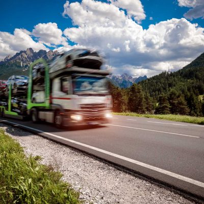 Truck trailer transports new cars rides on highway, Italy natural landscape Alps. Warning - authentic shooting there is a motion blur.